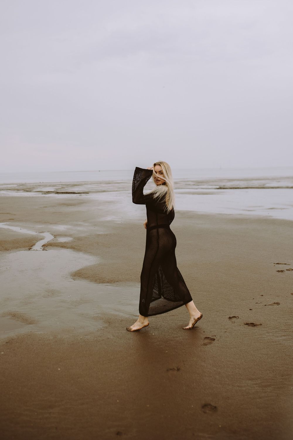A person in a long dark dress performs expressive dance movements on a misty beach in a sequence of artistic photos.
