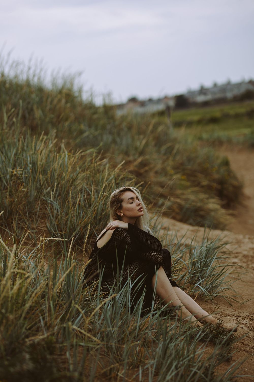 A person in dark clothing lies peacefully among tall grass on a hillside during golden hour.