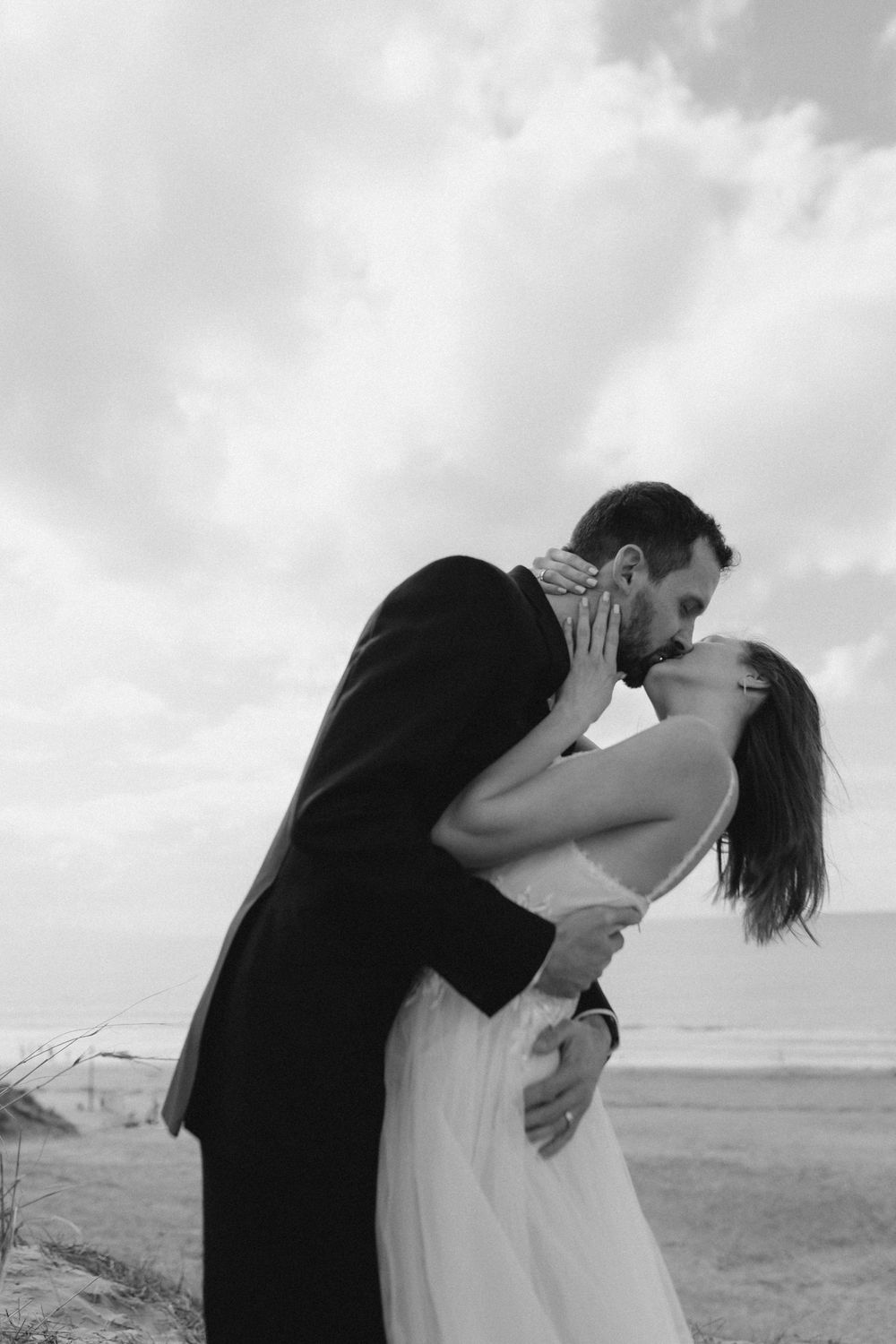 Romantic black and white photo sequence showing a couple embracing and kissing on a cloudy beach.