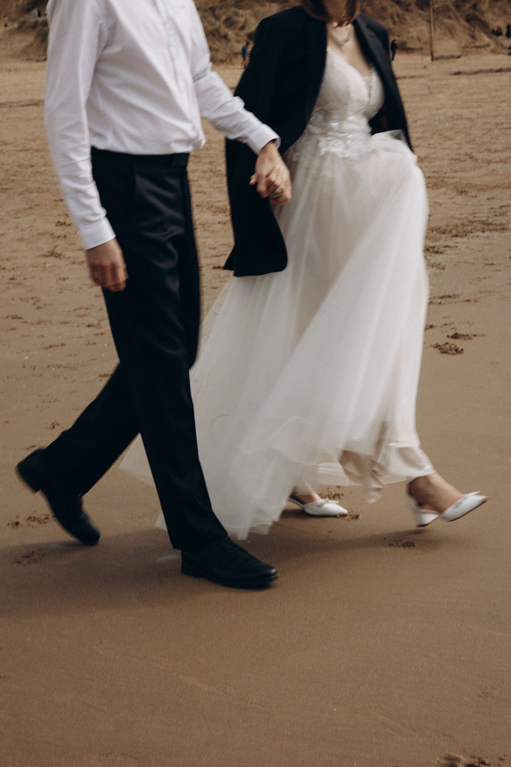 Cropped view of a bride and groom's feet walking together on a sandy beach.