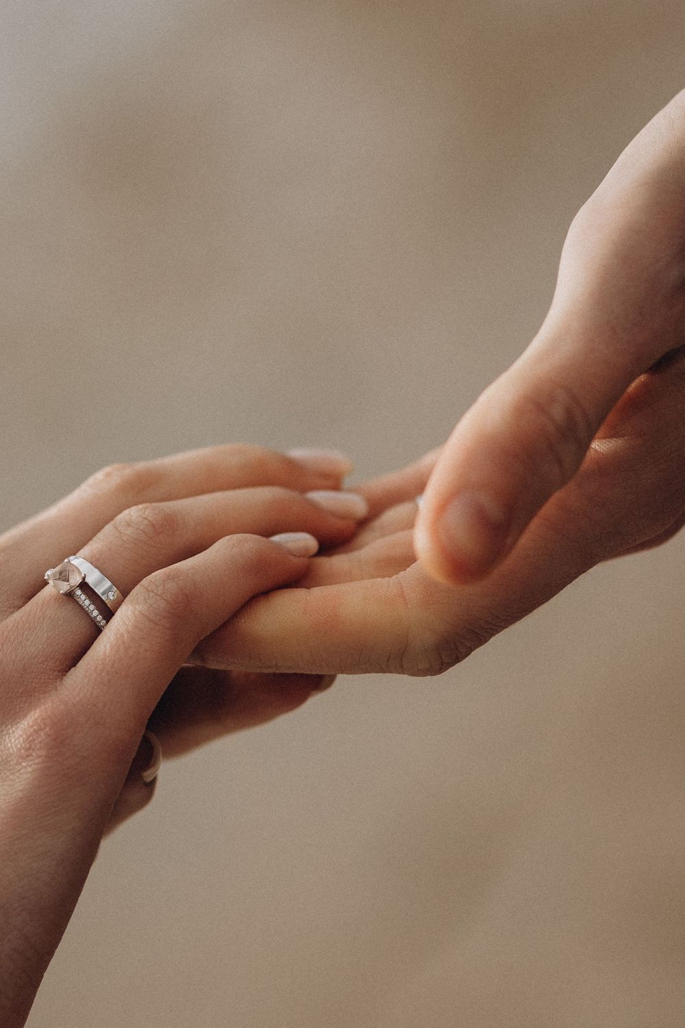 A series of hands reaching out to hold each other in a gentle, intimate gesture against a soft beige background.