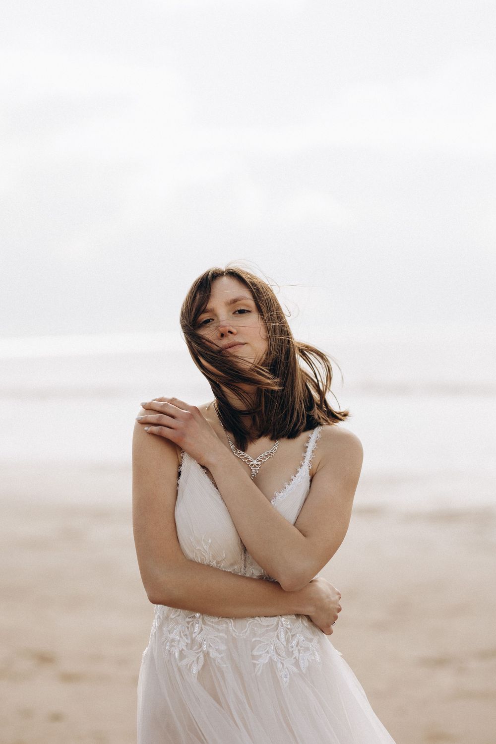 Ethereal portrait of someone in a white lace wedding dress with flowing hair on a misty beach.
