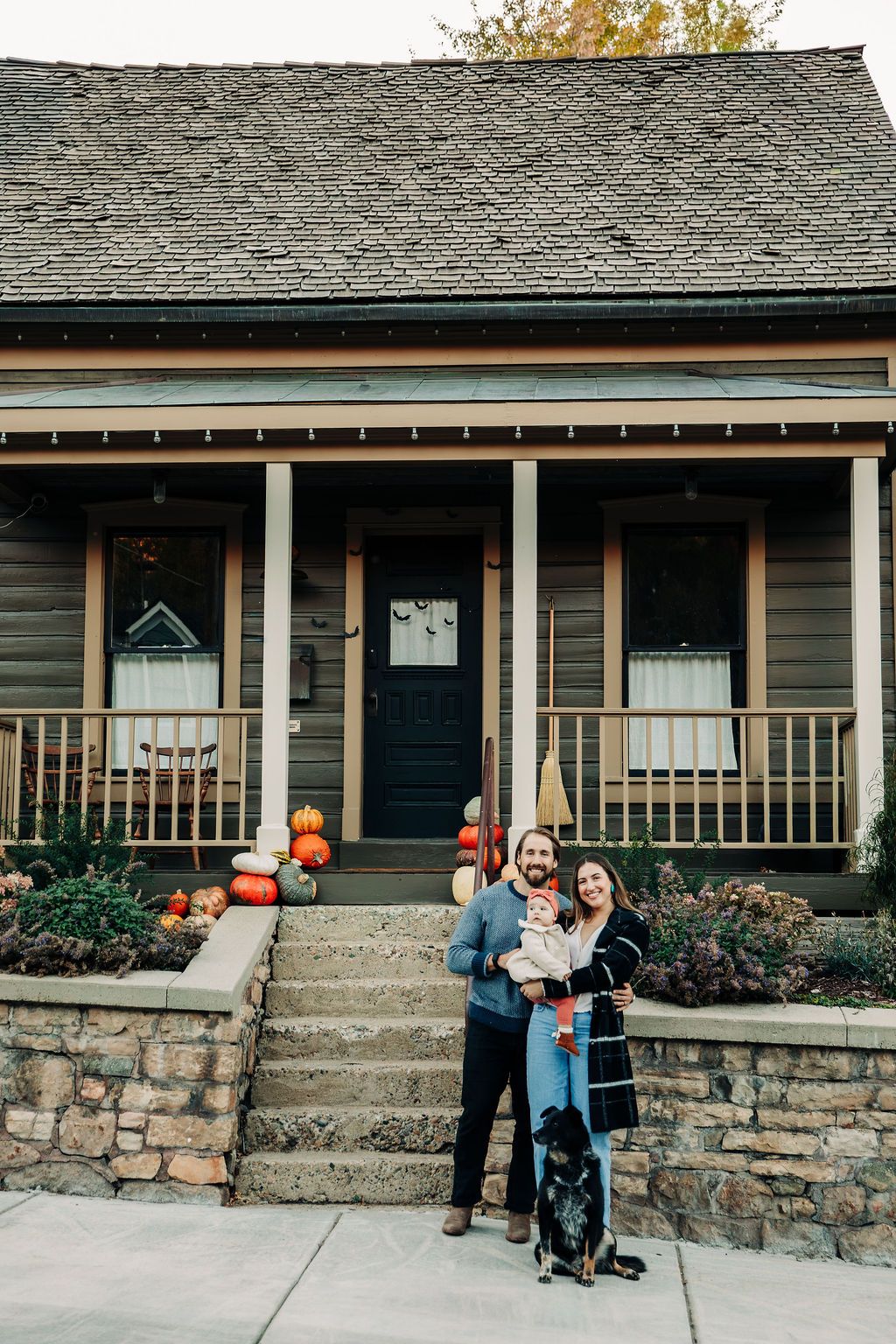 Family poses in front of rustic stone porch with autumn pumpkins decorating the steps.