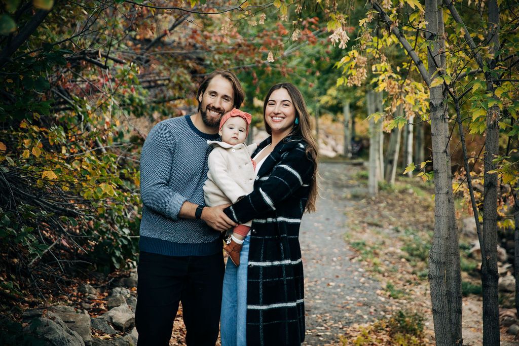 Family enjoying a tender moment together in a fall woodland setting with golden leaves.