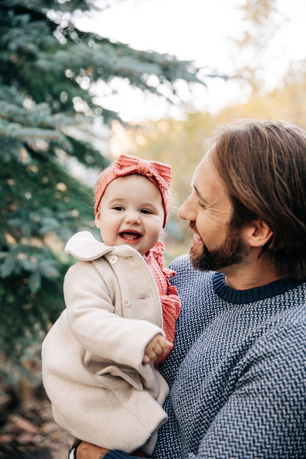 A joyful outdoor family moment captured with a baby in a cream coat and coral headband during autumn.
