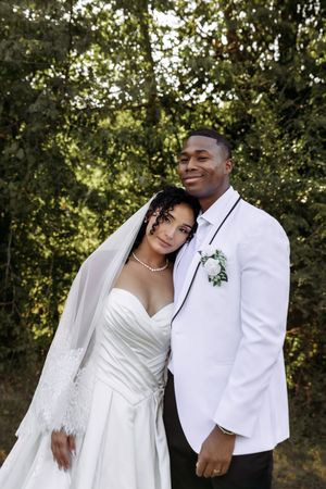 A loving embrace between newlyweds in white formal wear during their outdoor wedding photoshoot.