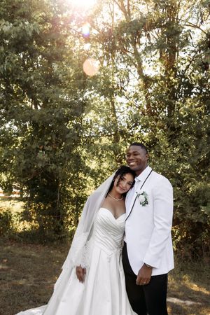 A sun-drenched wedding portrait featuring a couple in white against a leafy backdrop.