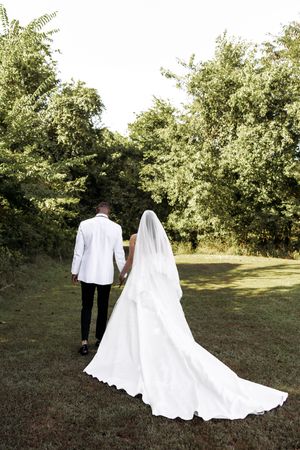 A wedding couple walking away showing the dramatic train of the white wedding dress against green foliage.