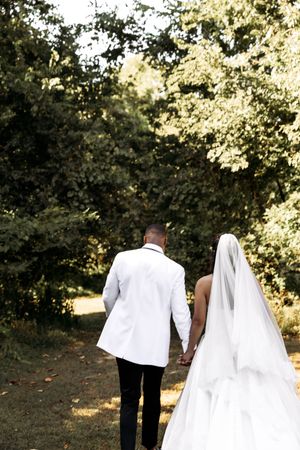 A candid wedding photo capturing a couple walking away in formal attire through a wooded setting.