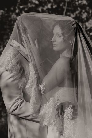 An artistic black and white wedding portrait captured through a sheer bridal veil.