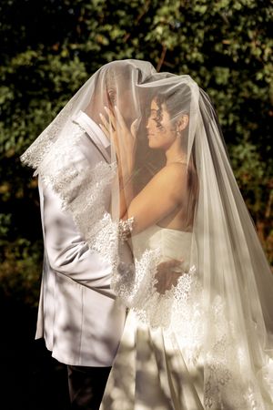 A romantic wedding portrait showing tender moments between newlyweds beneath flowing white veil.
