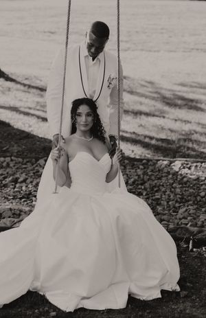 Black and white portrait of a bride on a swing in a flowing white wedding gown.