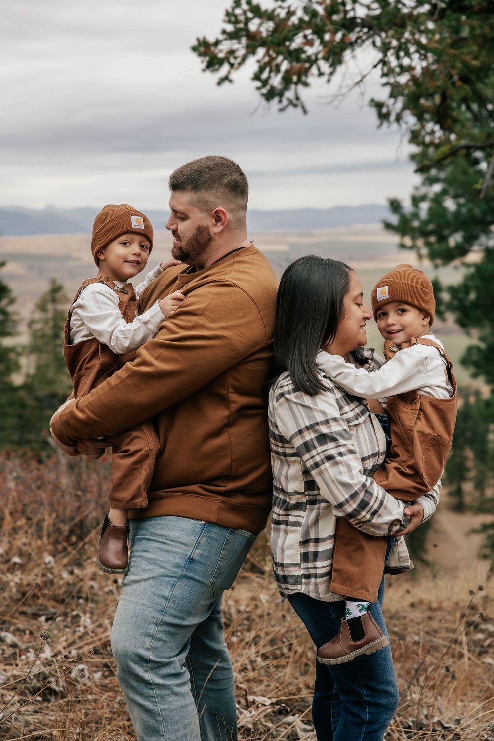 Family shares playful moments together outdoors wearing matching brown and plaid clothing.