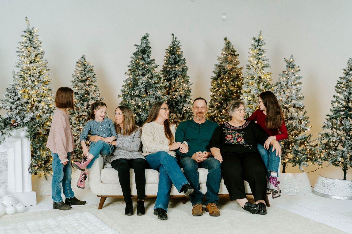 A series of casual holiday photos showing people sitting and posing in front of decorated Christmas trees.