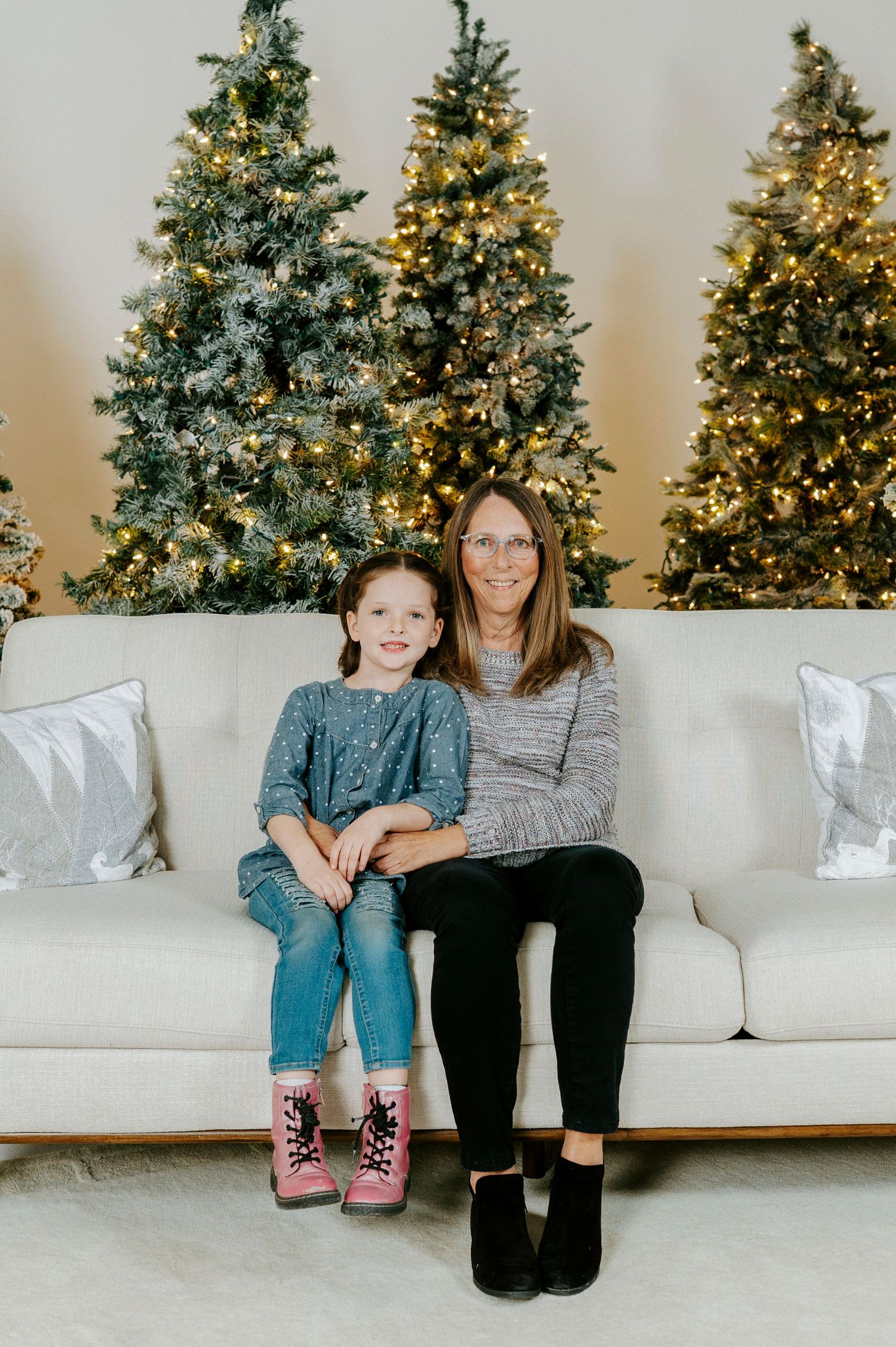 A white couch sits in front of multiple decorated Christmas trees with twinkling lights creating a festive holiday scene.