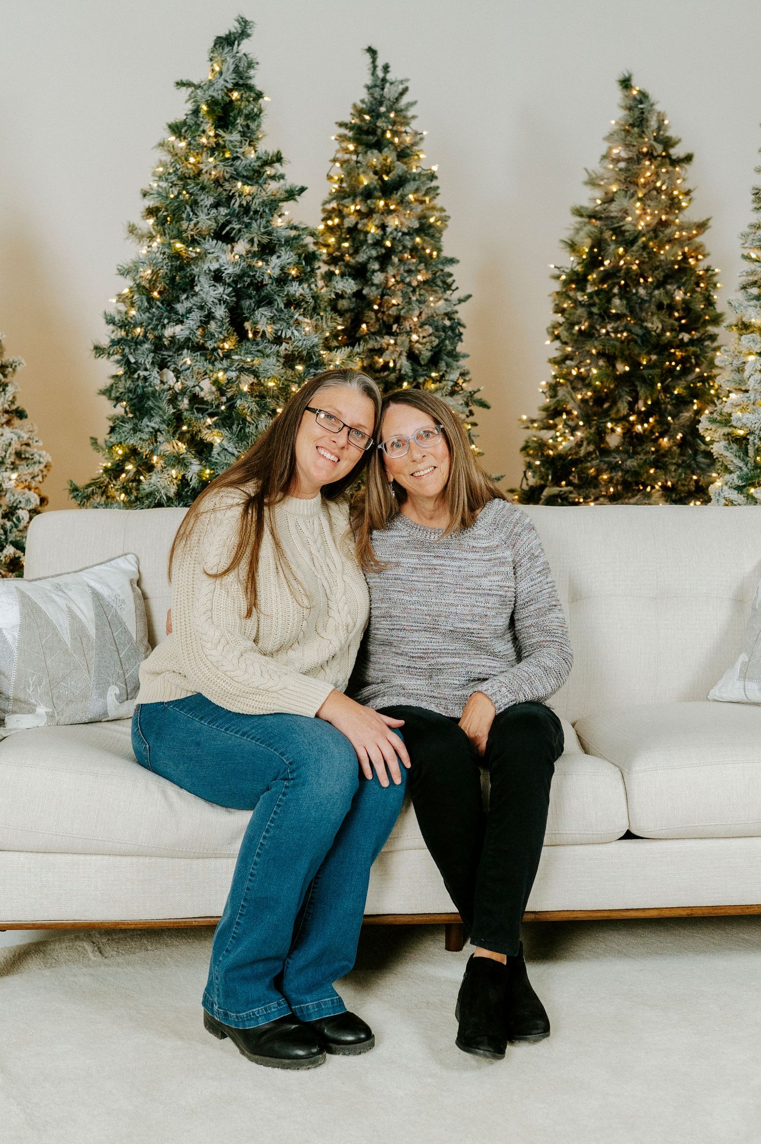 Two people sitting on a white couch with decorated Christmas trees in the background.