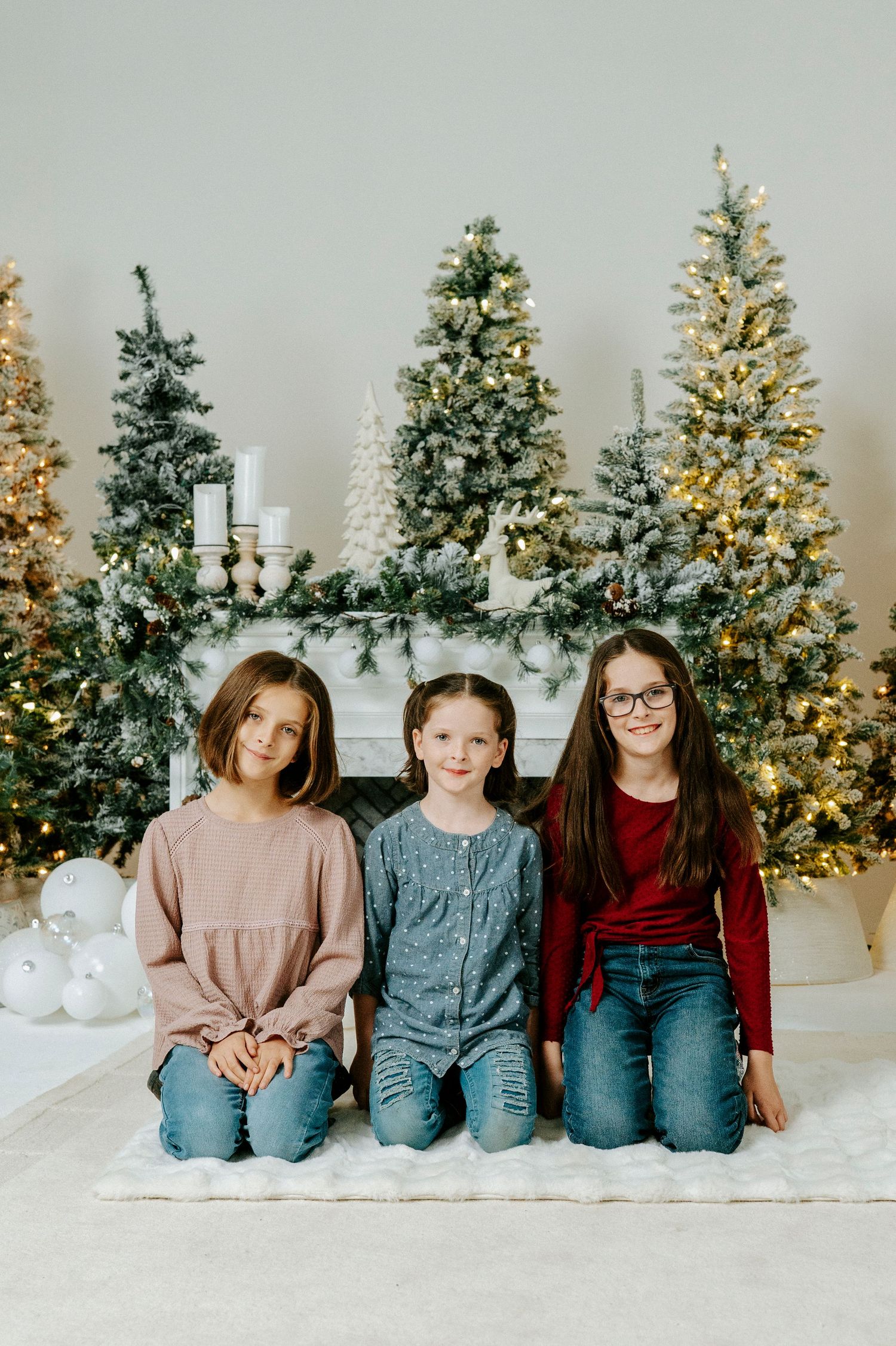 Progressive sequence of family members sitting on floor in front of multiple decorated Christmas trees in white room.