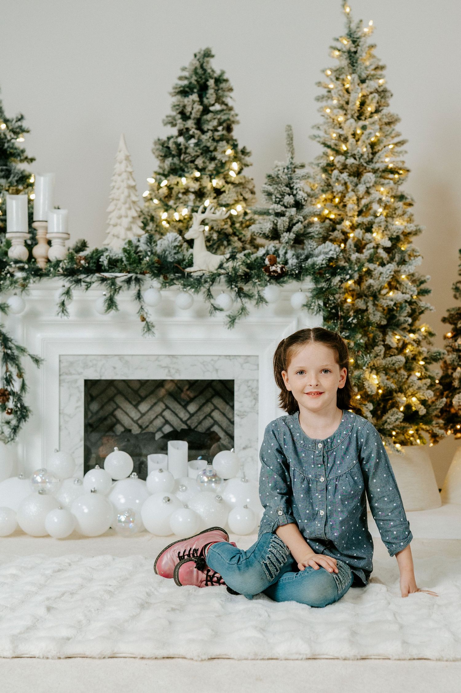 White Christmas scene with decorated trees, fireplace mantel, and soft white decor creating a cozy winter atmosphere.
