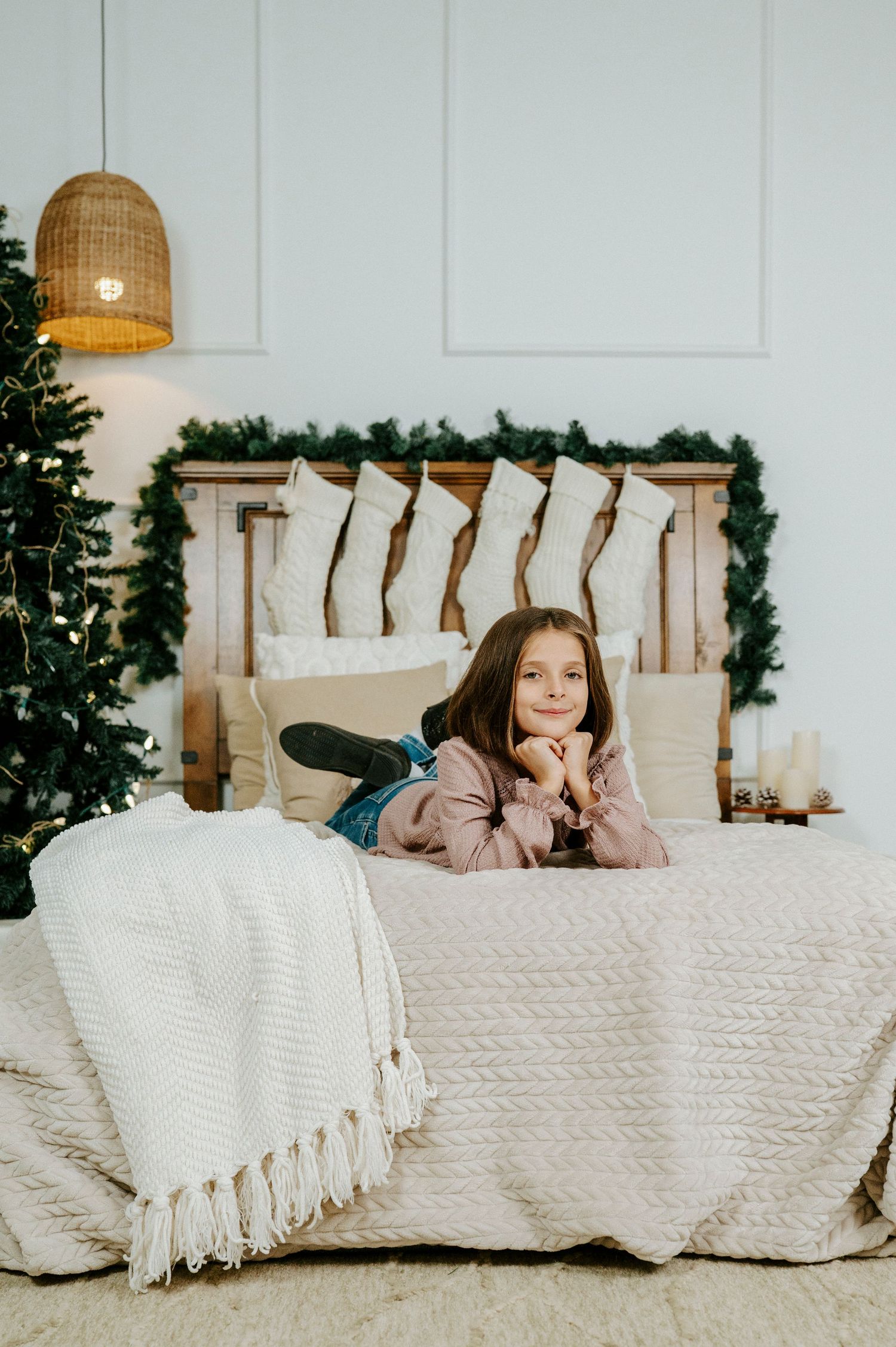 A cozy white blanket draped over a bed with decorative greenery and woven pendant lights in the background.