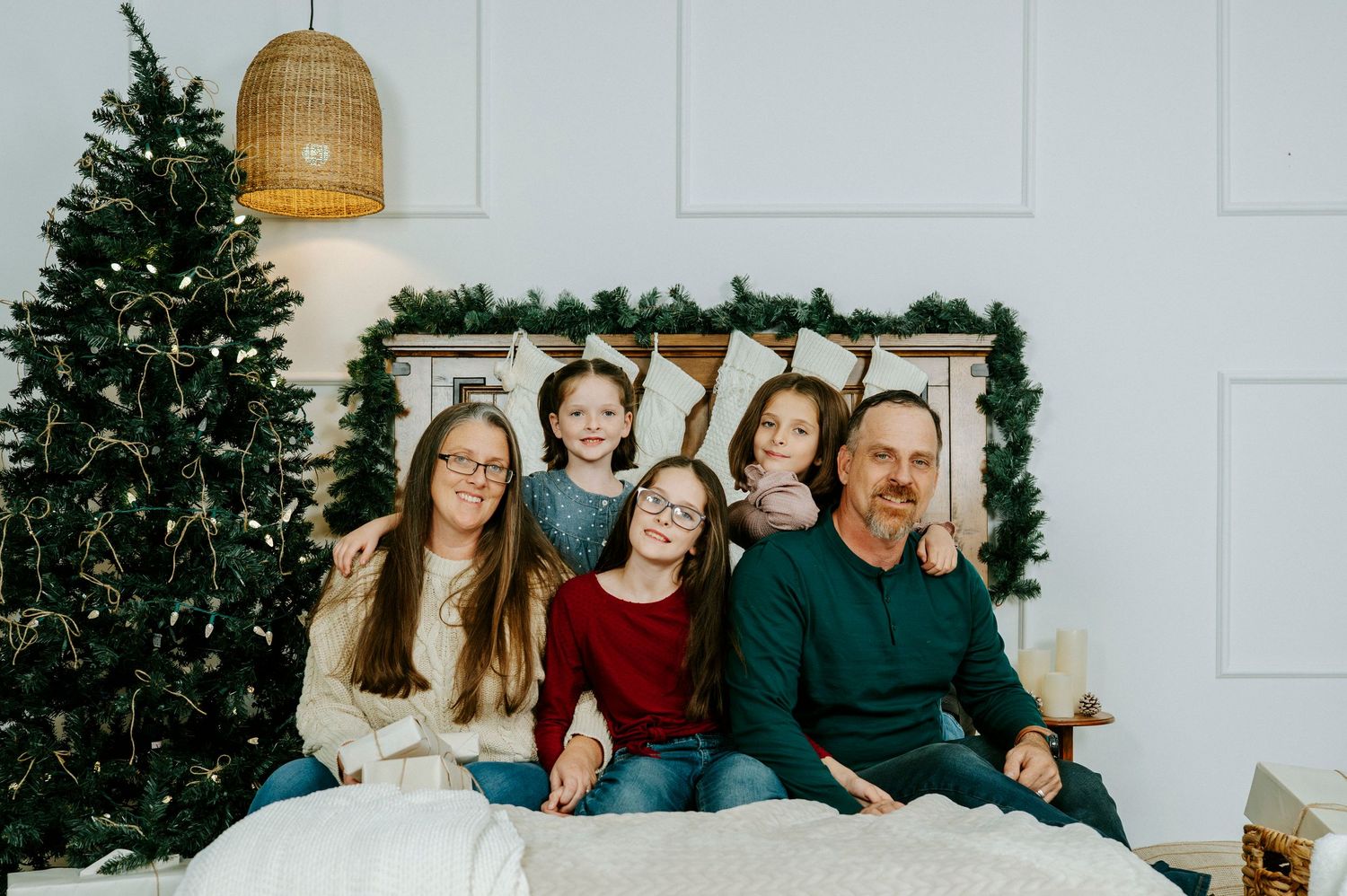 A family sits together on a white couch for a holiday photo with a Christmas tree and garland decorations in the background.