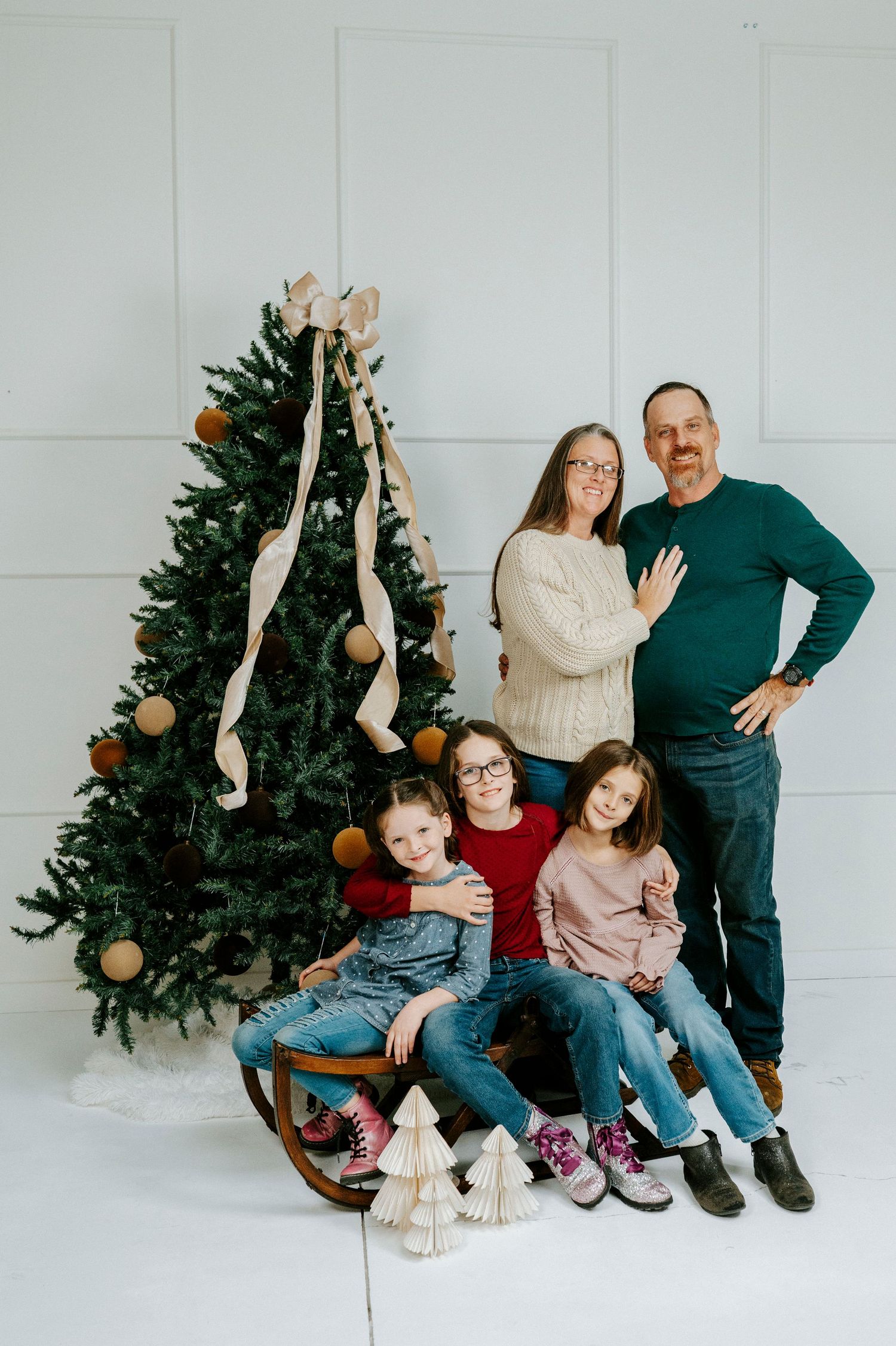 A family poses together in front of a Christmas tree in a series of candid holiday photos against a white wall.