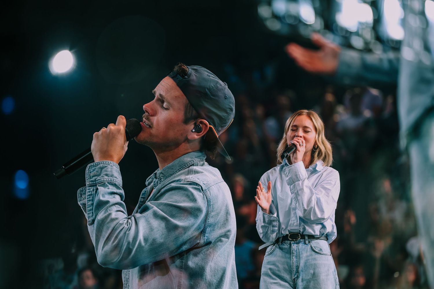 Two singers performing on stage with microphones at a live music concert event.