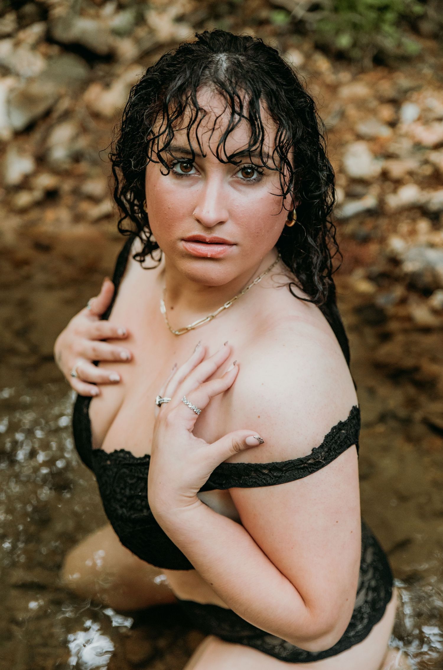 A woman in a black swimsuit poses in a natural stream surrounded by autumn leaves.