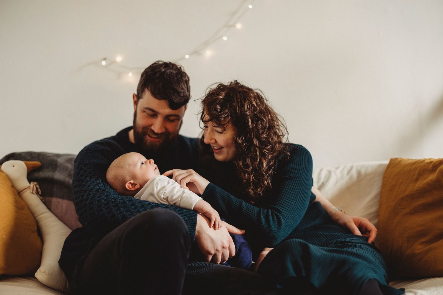 A couple relaxes on a brown couch with their baby in a tender family moment.