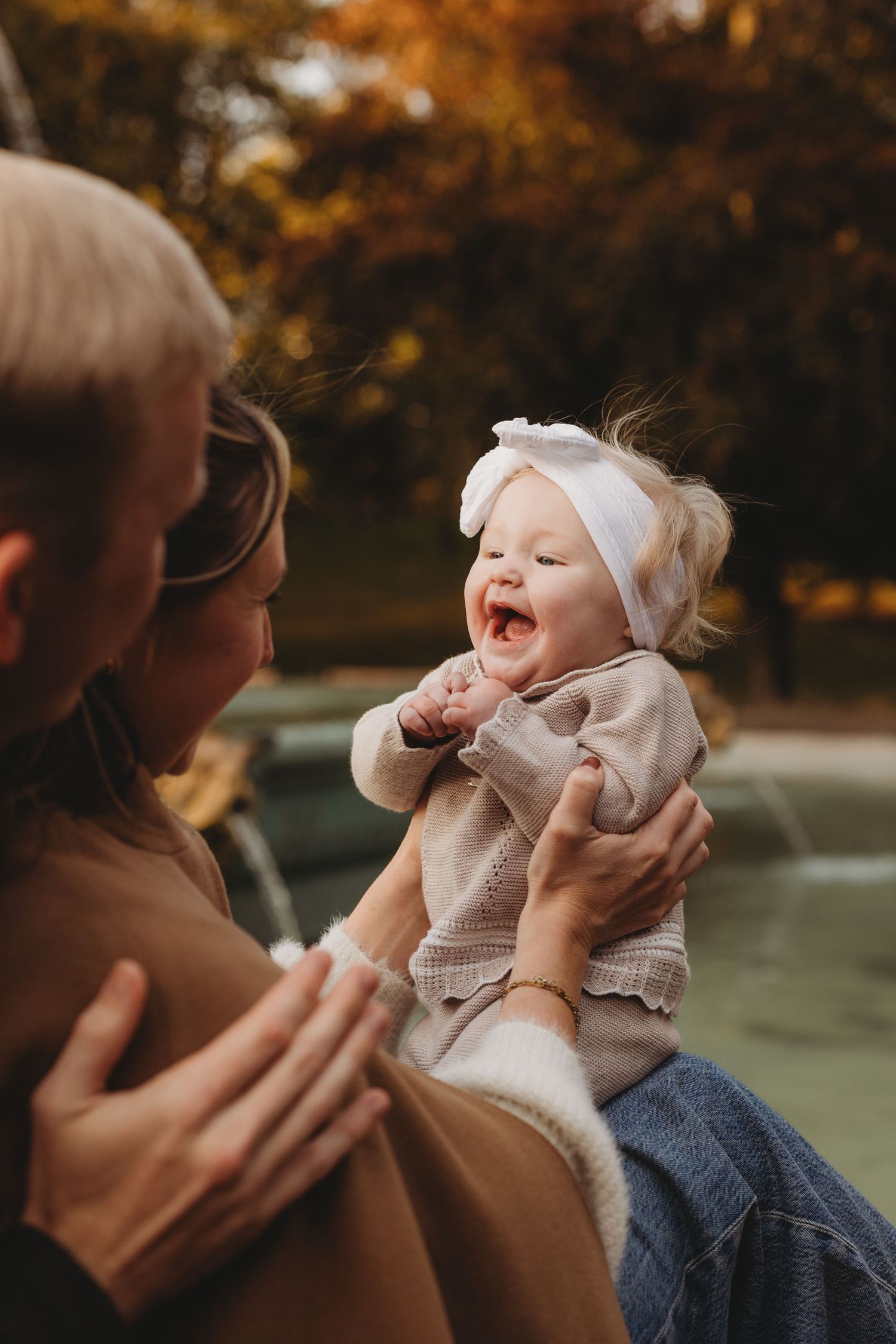 A parent plays and laughs with their baby outdoors during autumn while wearing cozy sweaters.