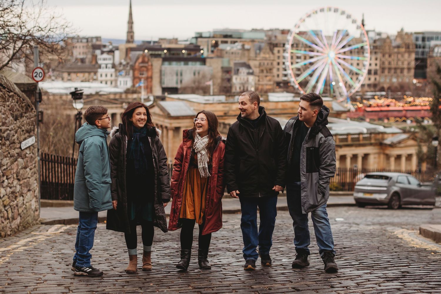 Family group wearing warm coats stands together on a cobblestone street during autumn.