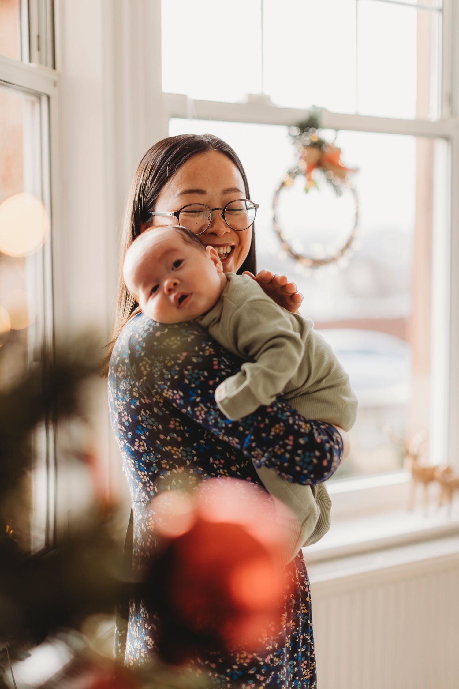 A heartwarming moment by a bright window as a parent and baby share joyful smiles in a cozy home setting.