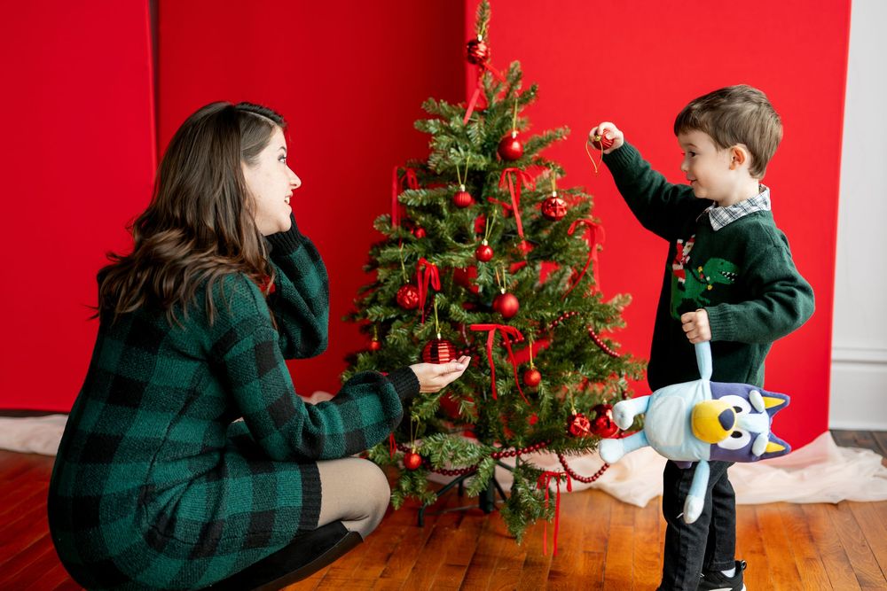 Mother and son decorating a Christmas tree together against a bold red wall.