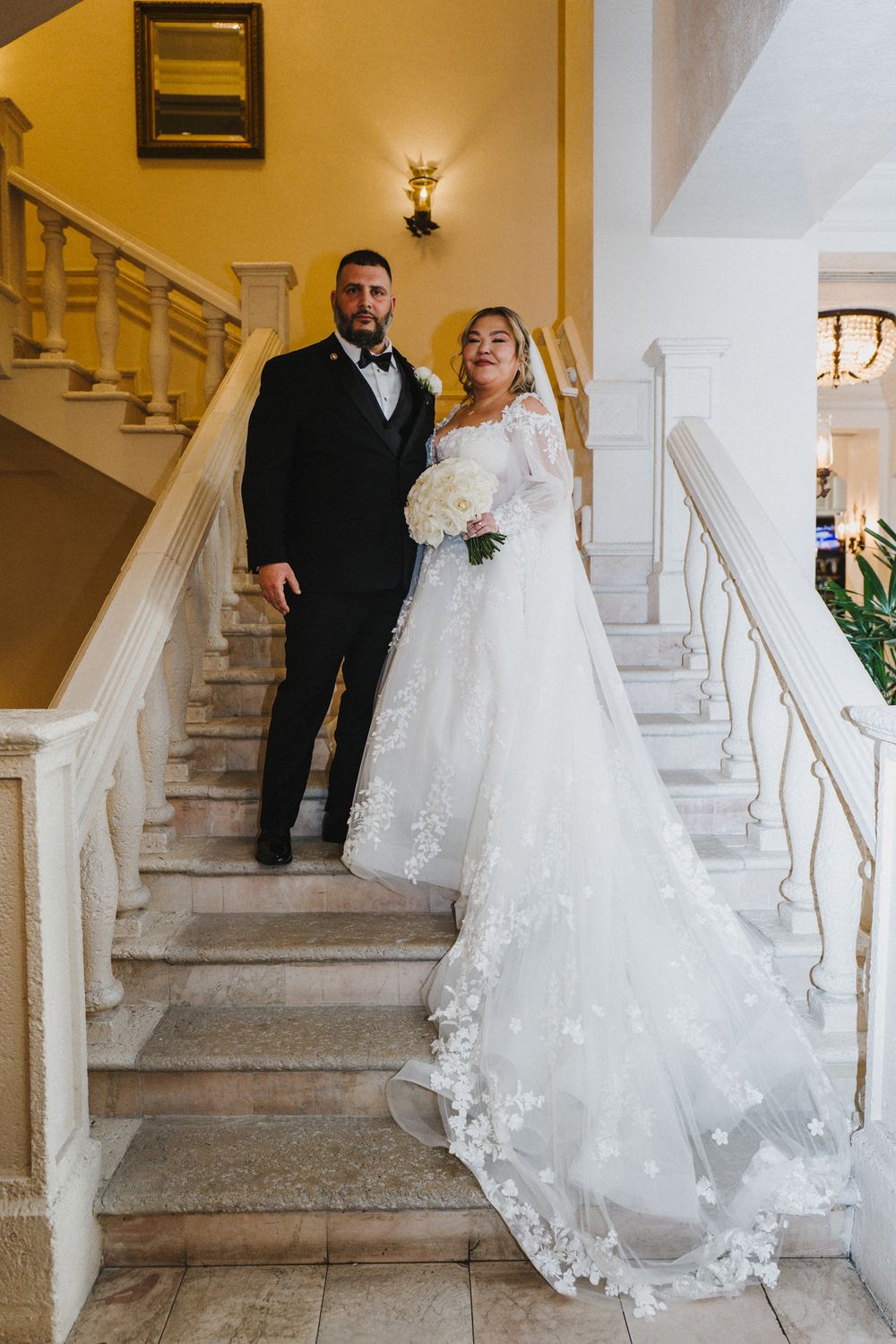 A couple in formal wedding attire descends an elegant white marble staircase in a series of romantic poses.