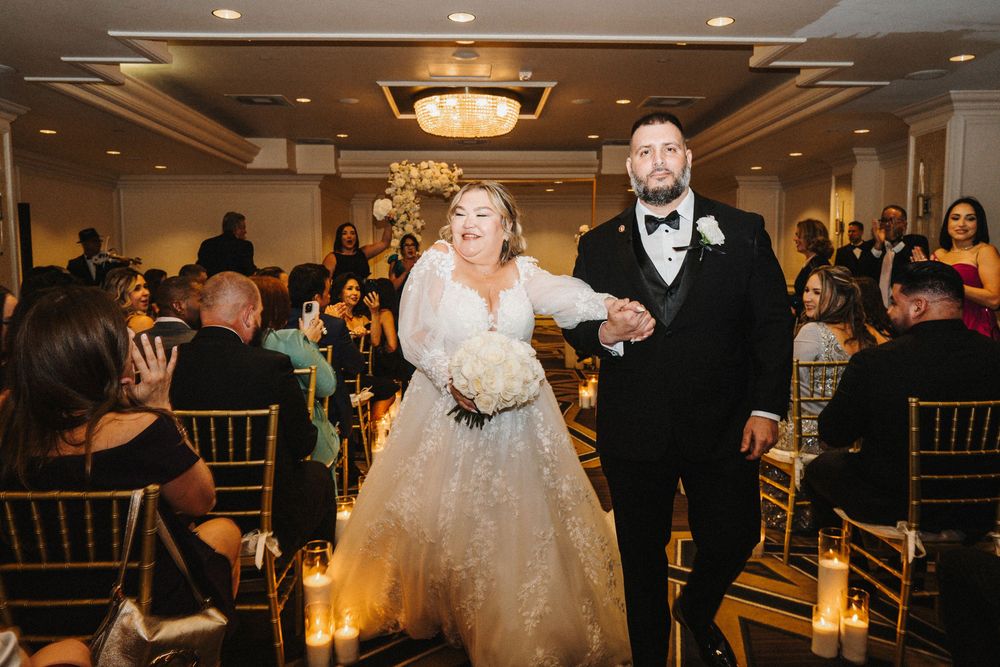 A joyful couple makes their grand entrance at their wedding reception as guests look on from decorated tables.