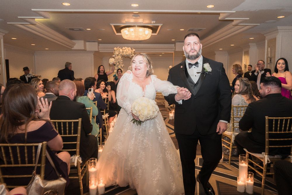 Bride and groom walking down the aisle hand in hand at elegant indoor wedding reception with candlelit decor.