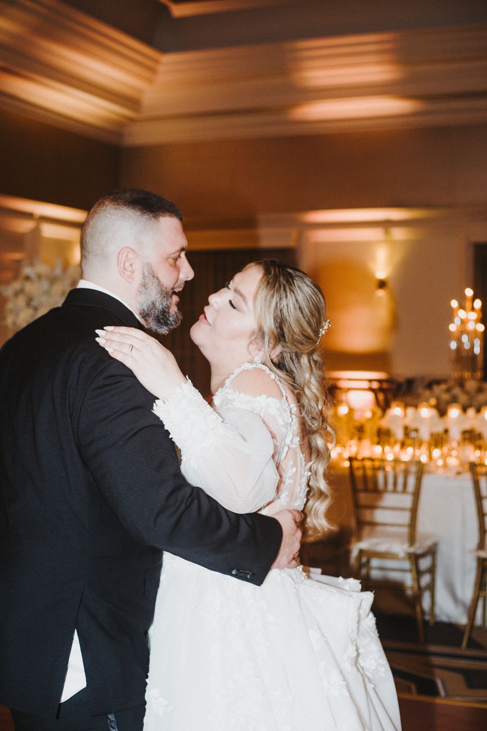 A romantic moment between newlyweds sharing their first dance in an elegantly lit ballroom reception venue.