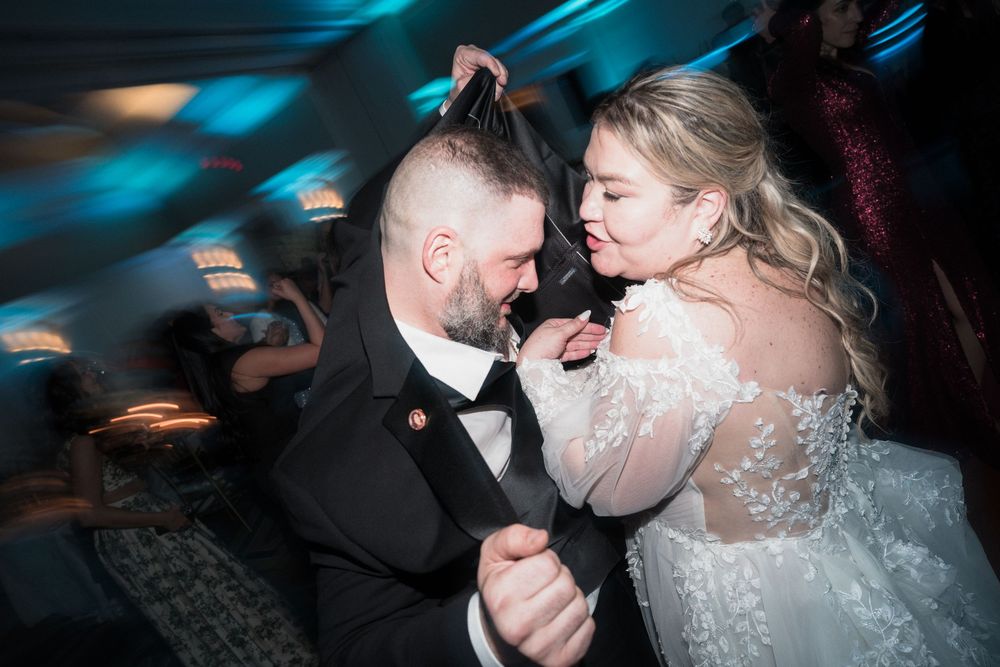 Bride and groom share a joyful dance together at their wedding reception under blue ambient lighting.