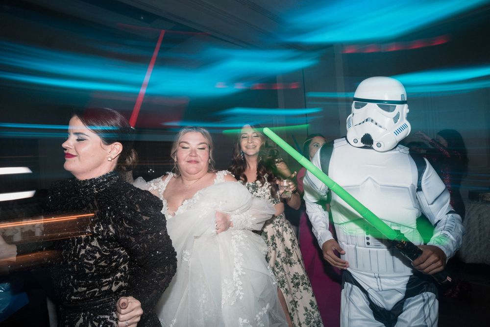 Bride dancing with Stormtrooper and guests wielding lightsabers at a Star Wars themed wedding reception.