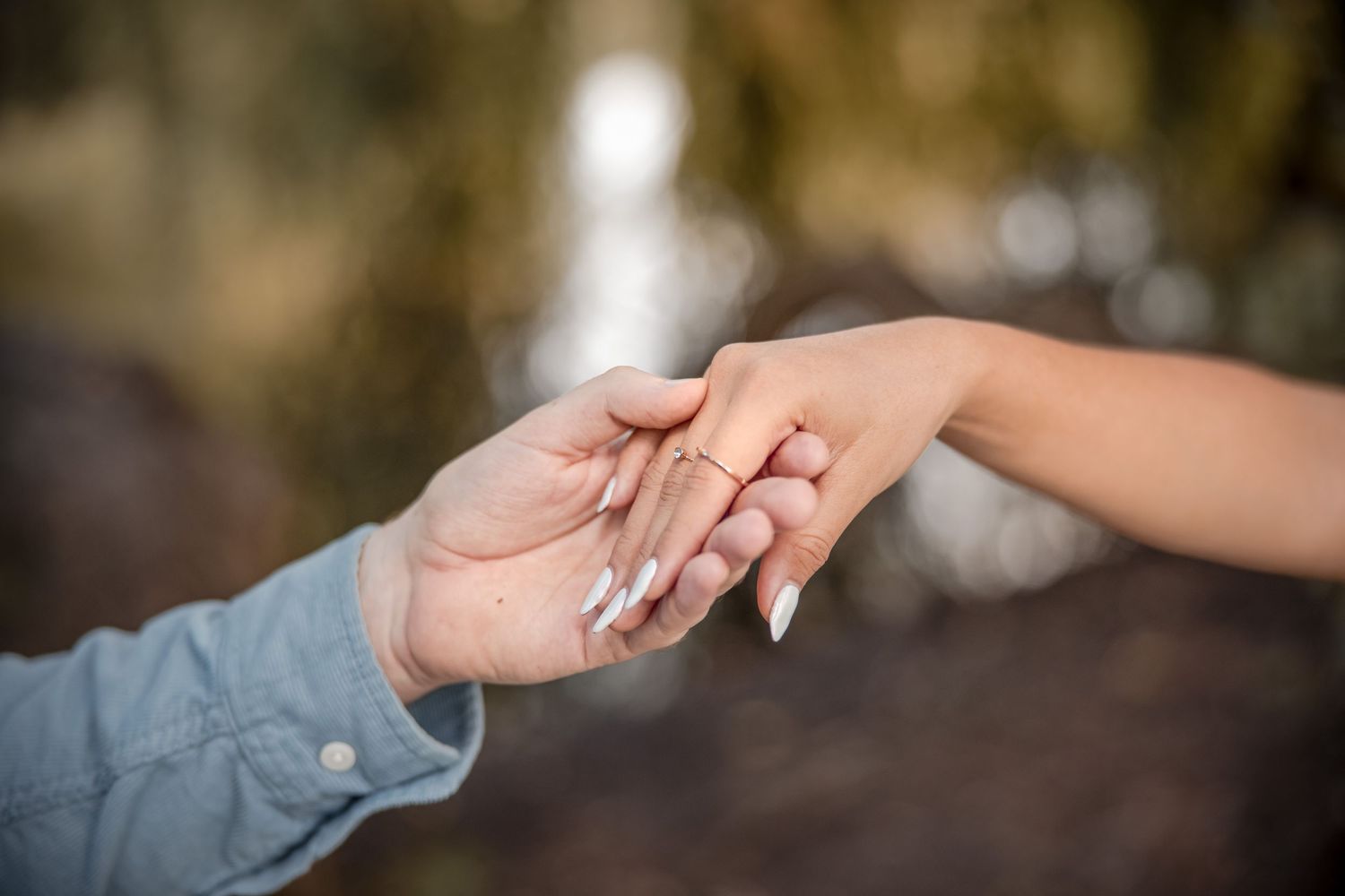 Two hands tenderly clasped together in a romantic moment with soft bokeh background.
