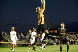 Soccer goalkeeper leaps high into the air to make a save during a nighttime match at a stadium.