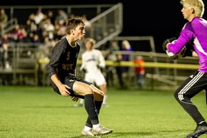 Soccer player in black uniform dribbles ball across field during nighttime match under stadium lights.
