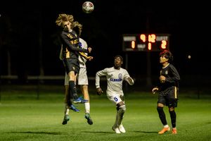 Soccer player jumps high to head the ball during a nighttime match on an illuminated field.