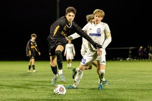 Soccer players compete for possession of the ball during a nighttime match on an illuminated field.