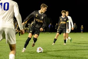 Soccer player in black uniform dribbles the ball during nighttime match on grass field.