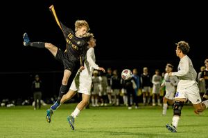 A soccer player performs a sliding tackle during a nighttime match on a grass field.
