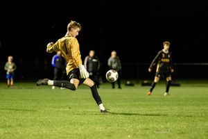 Soccer player in yellow uniform kicking ball during nighttime match on illuminated grass field.