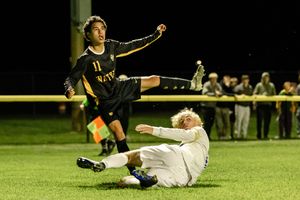 Soccer player slides on grass field to make a tackle during nighttime match under stadium lights.