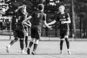 Soccer players in black uniforms compete for the ball during an intense match on a grass field.