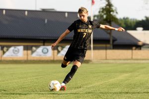 Soccer player in black uniform dribbles ball across green grass field during daytime practice.