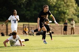 Soccer players compete for the ball during an intense match on a sunny grass field.